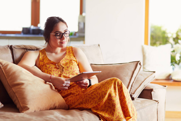 Beautiful young woman using tablet sitting on sofa at home at living room. - Foto, Imagem