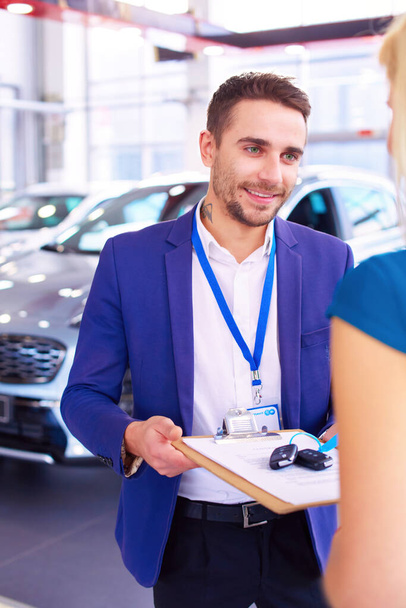 Car salesman sells a car to happy customer in car dealership and hands over the keys. - Фото, изображение