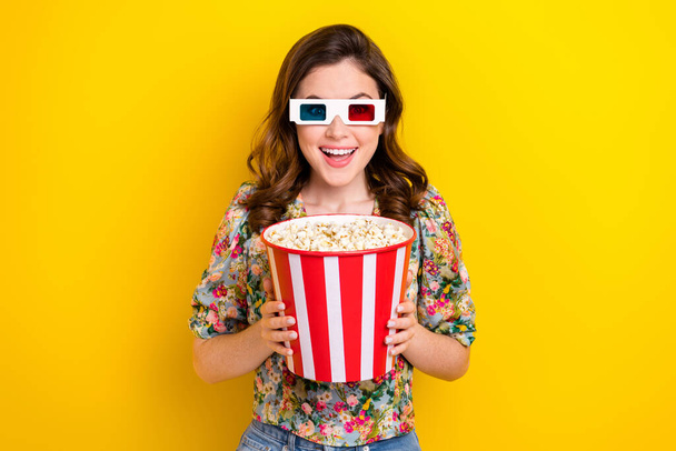 Photo of positive shocked girl hold big pop corn bucket enjoy 3d film in cinema isolated bright color background. - Foto, Bild