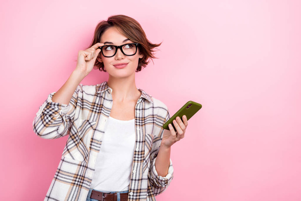 Portrait of thoughtful clever business lady wear plaid shirt smartphone looking interface new website options isolated on pink background. - Foto, imagen