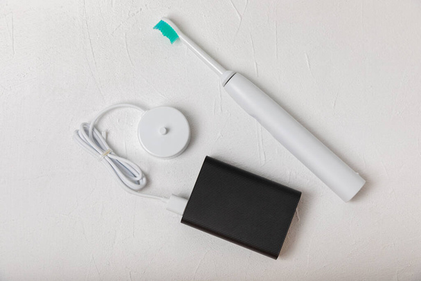 A modern electric toothbrush is being charged from an external power bank battery on a marble background. Modern home technology concept. Oral and gum care. Medicine concept. Dentist. - Foto, Imagem