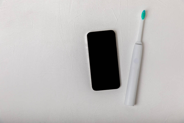 Sonische elektrische tandenborstel met draadloze verbinding met een smartphone app op een witte marmeren achtergrond. Modern huis technologie concept. Orale en tandvlees zorg. Medicijnconcept. Tandarts. - Foto, afbeelding