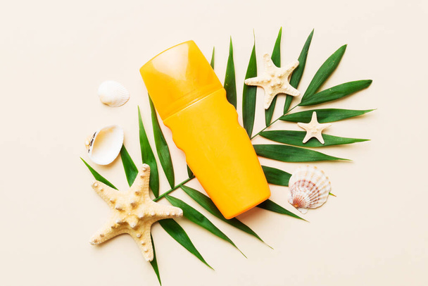 Sunscreen spray bottle. Bottle with sun protection cream and sea shells with tropical green leaf on color background, top view. - Fotografie, Obrázek