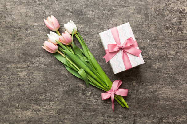 Pink tulips flowers and gift or present box on colored table background. Mothers Day, Birthday, Womens Day, celebration concept. Space for text top view. - Fotó, kép