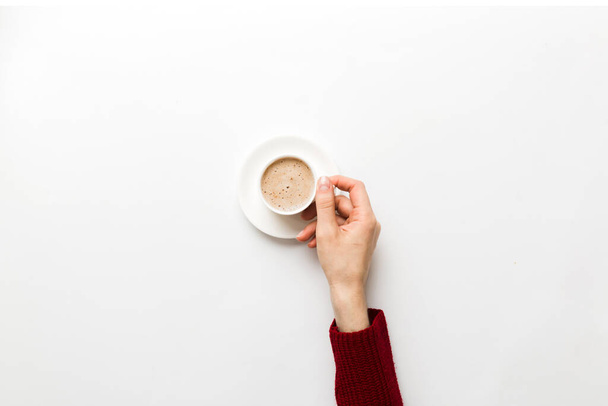 Minimalistic στυλ γυναίκα χέρι κρατώντας ένα φλιτζάνι καφέ σε έγχρωμο φόντο. Επίπεδο lay, κορυφαία θέα φλιτζάνι καπουτσίνο. Κενό μέρος για κείμενο, αντίγραφο χώρου. Εθισμός στον καφέ. Πάνω άποψη, επίπεδη lay. - Φωτογραφία, εικόνα