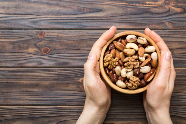 Woman hands holding a wooden bowl with mixed nuts Walnut, pistachios, almonds, hazelnuts and cashews. Healthy food and snack. Vegetarian snacks of different nuts. - Photo, Image