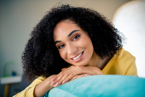 Photo of pleasant toothy beaming candid sincere woman with perming coiffure wear yellow long sleeve smiling on sofa at home room indoors. - Фото, изображение