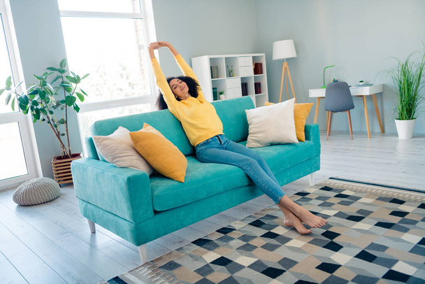 Muotokuva optimistinen rauhallinen tyytyväinen tyttö aaltoileva kampaus pukeutunut keltainen huppari venyttely sohvalla aamulla sisätiloissa huone. - Valokuva, kuva