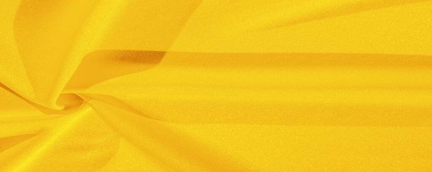 Gele zijde. Gladde elegante gele luxe zijden stof kan worden gebruikt als een abstracte achtergrond met kopieerruimte, close-up. kleurrijke textuur - Foto, afbeelding