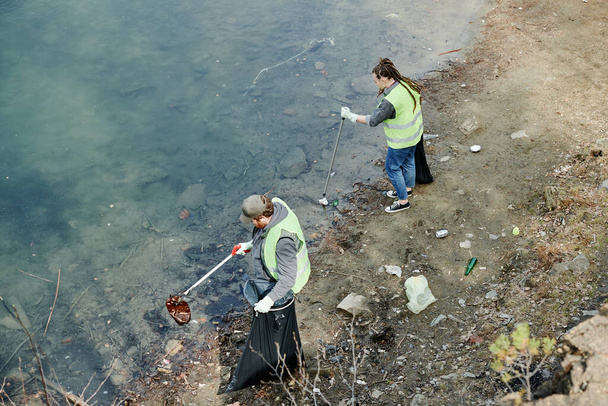 Gençler göl kıyısında çöp topluyor, yukarıdan bakıyorlar. - Fotoğraf, Görsel