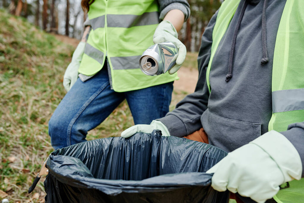 Εθελοντές βάζουν σκουπίδια που βρήκαν στο δάσος σε μια μεγάλη πλαστική σακούλα. - Φωτογραφία, εικόνα