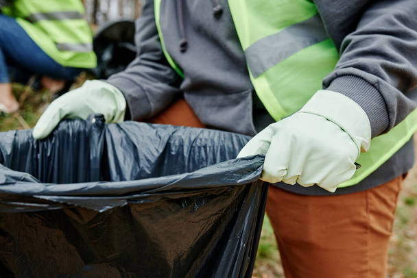 Immagine da vicino del volontario che tiene in mano un grosso sacco della spazzatura per la spazzatura raccolta nel parco cittadino - Foto, immagini