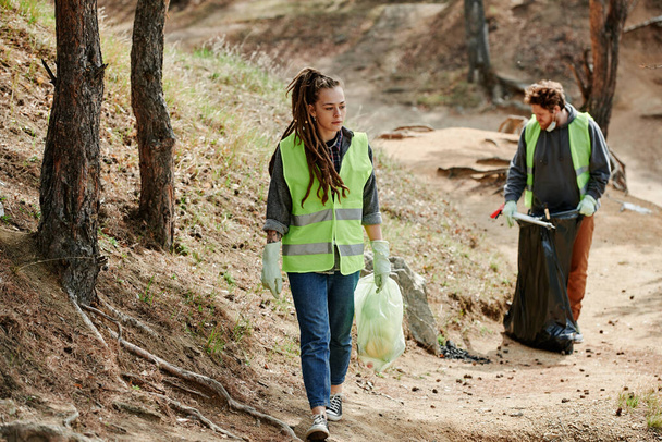 Young woman wearing neon green vest when collecting garbage in local park - Photo, Image