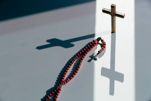 Ένα κομπολόι και ένας ξύλινος σταυρός του Πάσχα σύμβολο της Σταύρωσης του Χριστού με σκιά. Πίστη και θρησκεία έννοια.  - Φωτογραφία, εικόνα