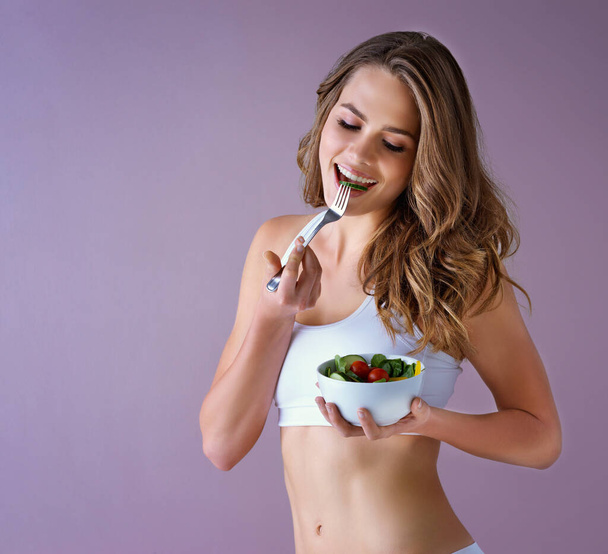 Їжте відповідно до ваших цілей. Студійний знімок здорової молодої жінки, що їсть салат на фіолетовому фоні
 - Фото, зображення
