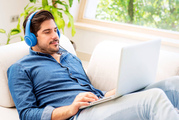 Caucasian middle aged man with headphone using a laptop and listening music at home.  - Foto, Bild