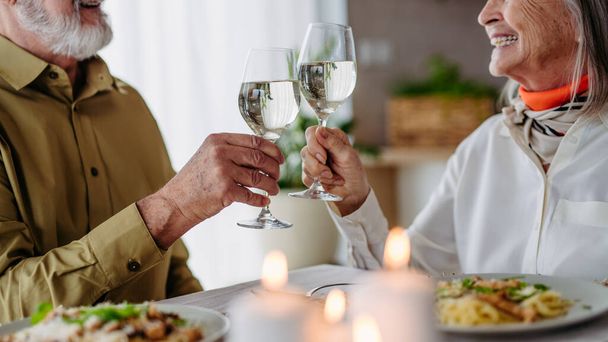 Senior man with his wife celebrating anniversary. Eldery couple having a romantic dinner, making cheers with wine glasses. - Foto, imagen