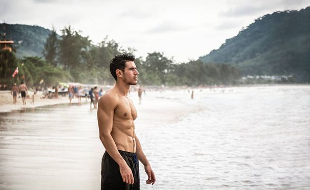 Half body shot of a handsome young man standing on a beach in Phuket Island, Thailand, shirtless wearing boxer shorts, showing muscular fit body - Foto, immagini
