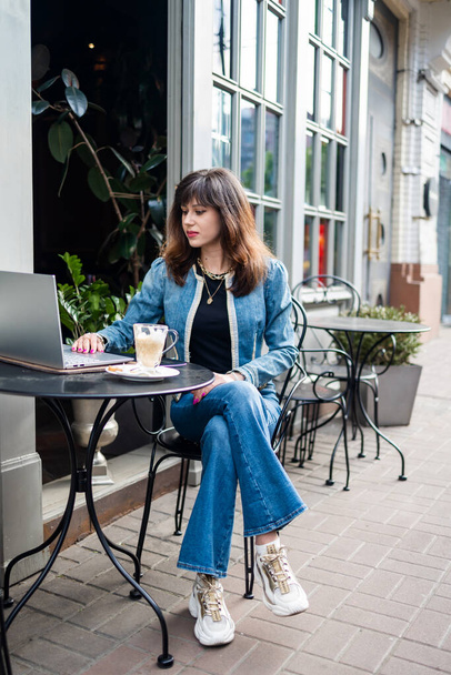 Mulher jovem, nômade digital trabalhando remotamente de um café, bebendo café e usando laptop. - Foto, Imagem