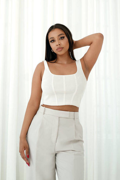 Young woman posing on white curtains background. Casual, fashionable mixed-race girl. Gorgeous model looking at camera.  - Φωτογραφία, εικόνα