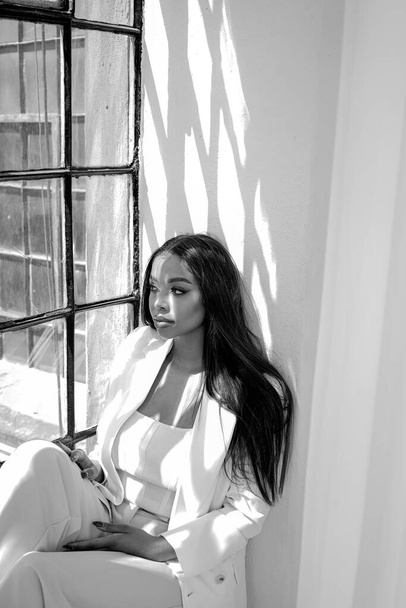 Elegant, fashionable young woman with long hair sitting near the window, relaxing during work day.  Mental health and work life balance concept. Black and white photo. - Foto, Imagem