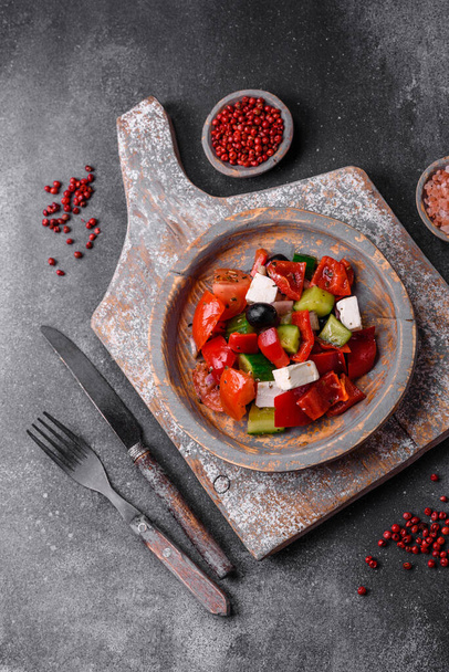 Delicious fresh juicy greek salad with feta cheese, olives, peppers, tomatoes, cucumber and onions on a gray concrete background - Photo, Image