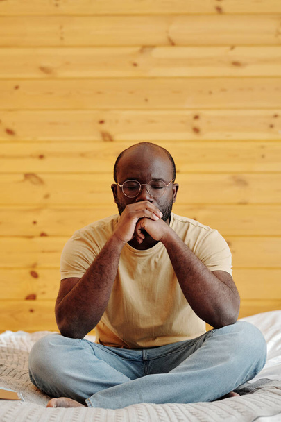 Молодий афроамериканець, що сидить на ліжку і глибоко зосереджується на своїх думках, щоб вирішити якусь проблему. - Фото, зображення