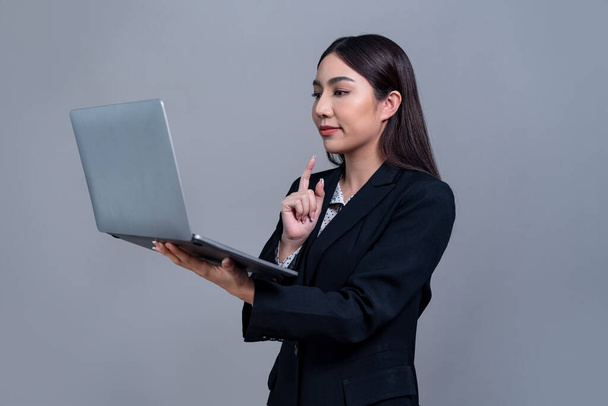 Confident young Asian businesswoman posing with laptop on isolated background. Office lady make hand holding gesture for promotions sales, technology advertisements or HR recruitment image. Jubilant - Photo, Image
