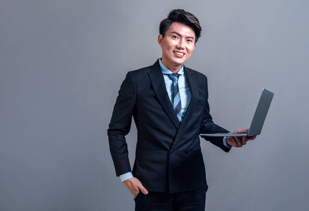 Jeune homme d'affaires asiatique confiant posant avec un ordinateur portable sur fond isolé. Les employés de bureau font un geste de prise de main pour des publicités de produits innovantes, des ventes promotionnelles ou le recrutement des RH. Jubilatoire - Photo, image