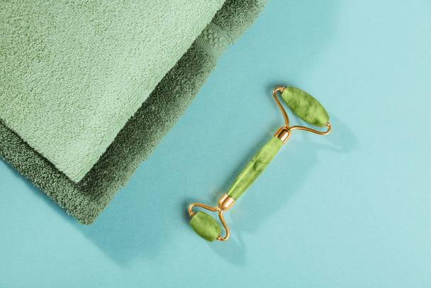 Massage roller for the face with two heads of jade stone and green leaves on light blue background. Beauty facial massage therapy, SPA self care concept. - Fotografie, Obrázek