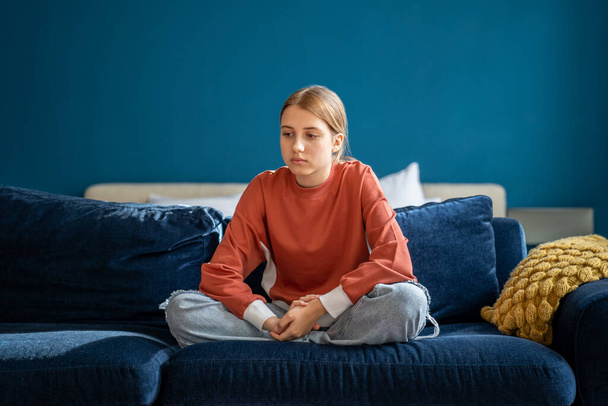 Upset moody teen girl sitting on sofa at home, being sad. Worried depressed adolescent child feeling lonely and frustrated, thinking about problems in school. Teenage mood swings - Foto, Imagen