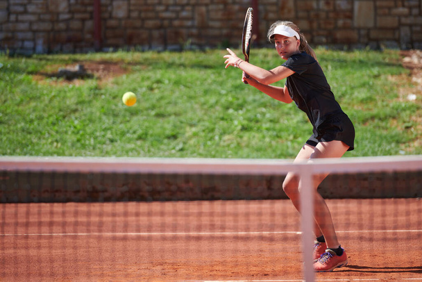 A young girl showing professional tennis skills in a competitive match on a sunny day, surrounded by the modern aesthetics of a tennis court - Foto, imagen