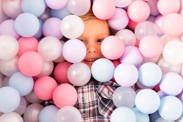 Little boy in a pool filled with plastic balls. Child peeking from pastel multi colored plastic balls for kids. top view. - Photo, Image