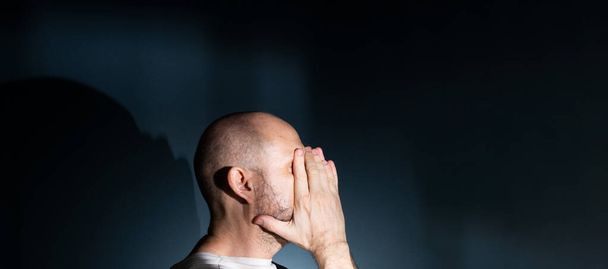 Trauriger Mann mit Kopfschmerzen oder Migräne. Gestresster Typ mit schmerzhaftem Gesichtsausdruck, der sich schrecklich schwach oder depressiv fühlt. Isoliert auf dunklem Hintergrund. - Foto, Bild