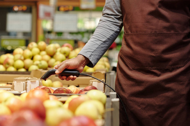 Крупный план молодого афроамериканского продавца, сканирующего свежие спелые яблоки в огромных коробках, движущегося вдоль витрины в продуктовом магазине - Фото, изображение