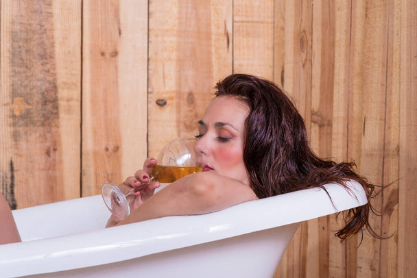 bela mulher dentro de uma banheira branca velha com uma bebida na mão relaxante descansando - Foto, Imagem
