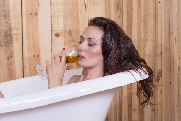 hermosa mujer dentro de una vieja bañera blanca con una bebida en la mano descansando relajante - Foto, imagen