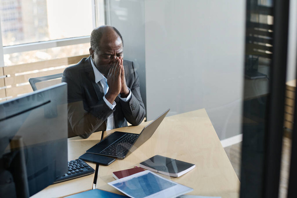 Empresário maduro estressado com as mãos juntas pela cara olhando para a tela do laptop enquanto sentado no local de trabalho em seu escritório - Foto, Imagem