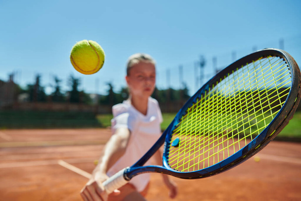 Close up photo of a young girl showing professional tennis skills in a competitive match on a sunny day, surrounded by the modern aesthetics of a tennis court - Zdjęcie, obraz
