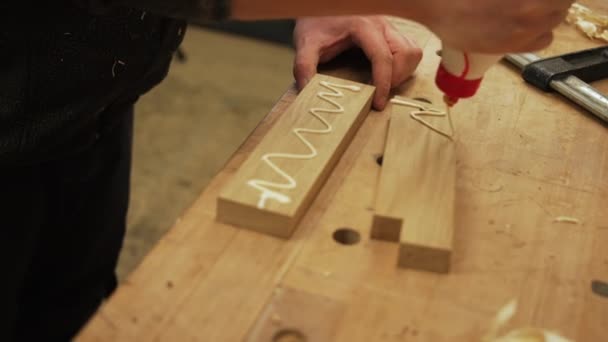 Timmerman knijpt lijm op houten stukken uit een fles om stukken aan elkaar te plakken. Hoge kwaliteit 4k beeldmateriaal - Video