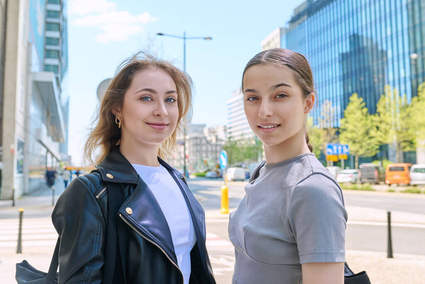 Two smiling teenage female students looking at camera, urban modern background. Youth, city, lifestyle, girls high school college age - Foto, Imagen