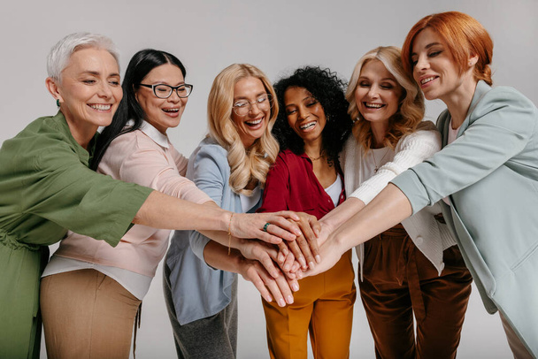 Multi-ethnic group of happy mature women holding hands together against grey background - Фото, изображение