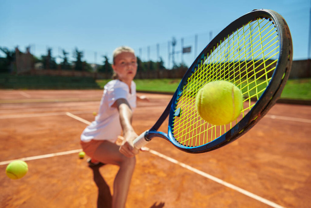 Close up photo of a young girl showing professional tennis skills in a competitive match on a sunny day, surrounded by the modern aesthetics of a tennis court - Foto, Imagem