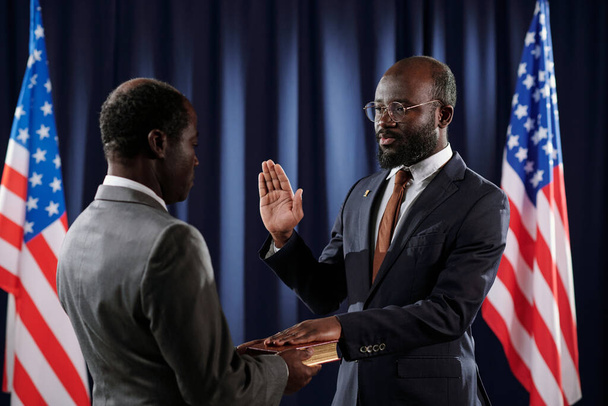 Joven presidente confiado de los Estados Unidos dando juramento de cargo durante la ceremonia de inauguración con la palma abierta y la mano izquierda en la Sagrada Biblia - Foto, imagen