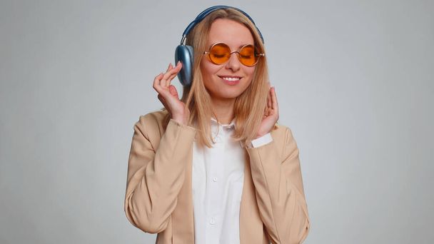 Happy business woman in headphones listening music and dancing disco fooling around having fun expressive gesticulating hands, relaxing on party. Girl isolated alone on studio gray wall background - Photo, Image