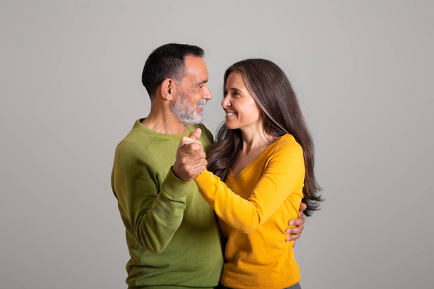Usmívající se šťastný evropský starý manžel a manželka mají rande, tančí spolu na šedém pozadí studia, kopírovat prostor. Rodinný vztah, romantika a pozitivní životní styl ve volném čase - Fotografie, Obrázek