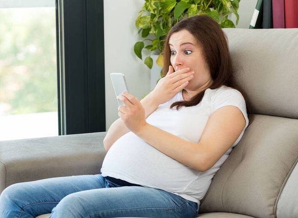 Shot of a amazed pregnant woman receiving shocking new at home - Foto, Bild