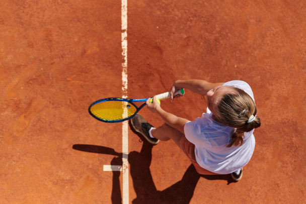 Top view of a professional female tennis player serves the tennis ball on the court with precision and power.  - Foto, afbeelding