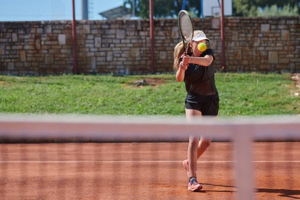 A young girl showing professional tennis skills in a competitive match on a sunny day, surrounded by the modern aesthetics of a tennis court - 写真・画像