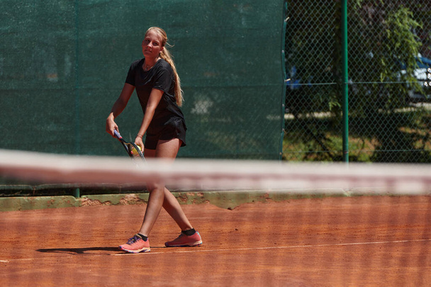 Nuori tyttö osoittaa tennistaitoja kilpailukykyisessä ottelussa aurinkoisena päivänä tenniskentän modernin estetiikan ympäröimänä. - Valokuva, kuva